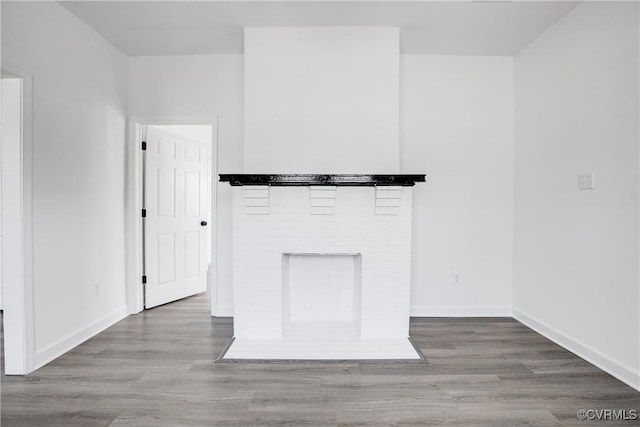 unfurnished living room with a brick fireplace, wood finished floors, and baseboards