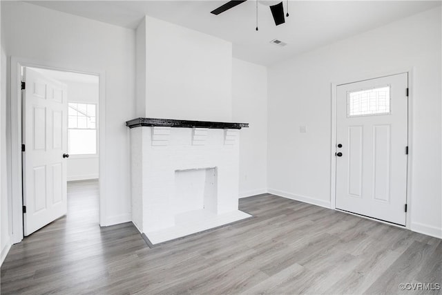 unfurnished living room featuring a fireplace, wood finished floors, visible vents, and a ceiling fan