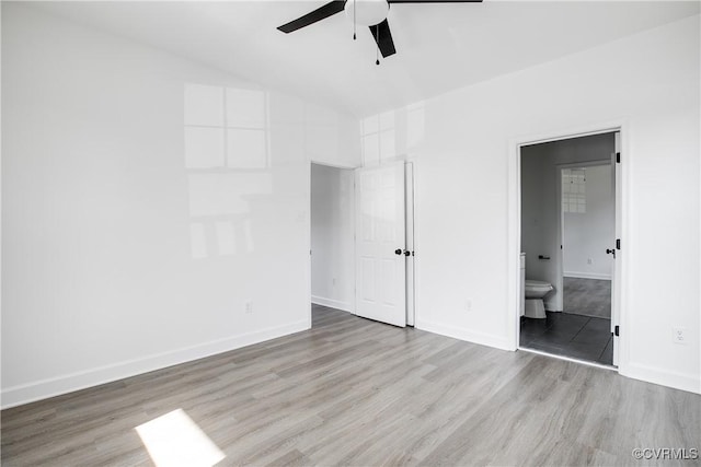 unfurnished bedroom with a ceiling fan, vaulted ceiling, ensuite bath, wood finished floors, and baseboards