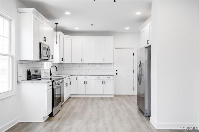 kitchen with a sink, appliances with stainless steel finishes, light wood-type flooring, backsplash, and light stone countertops