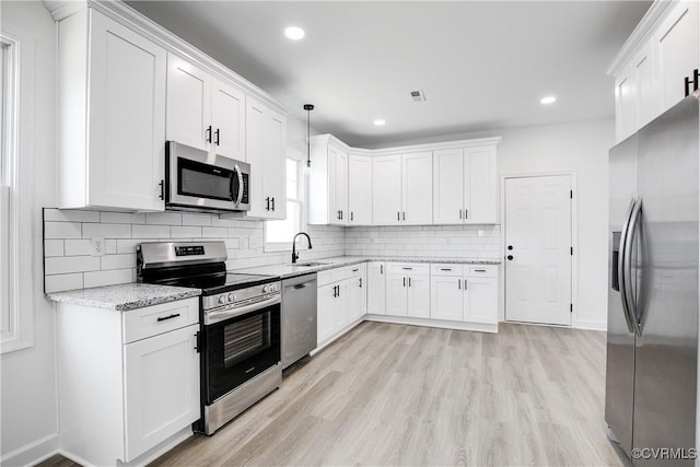 kitchen with light stone counters, stainless steel appliances, white cabinets, a sink, and light wood-type flooring