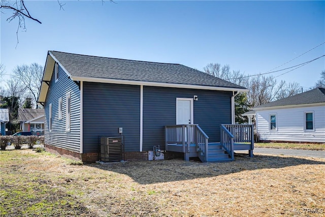 rear view of property featuring central air condition unit and roof with shingles