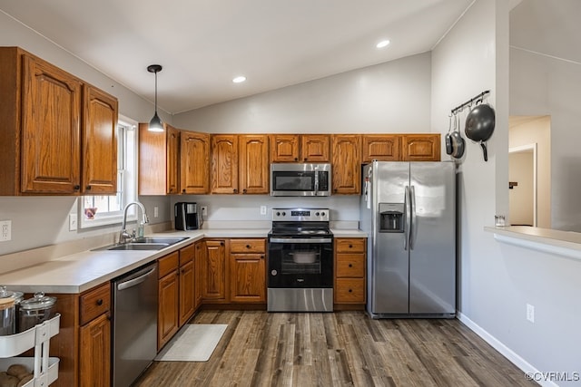 kitchen featuring appliances with stainless steel finishes, vaulted ceiling, brown cabinets, and a sink