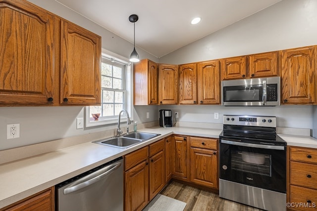 kitchen with lofted ceiling, a sink, light countertops, appliances with stainless steel finishes, and brown cabinetry