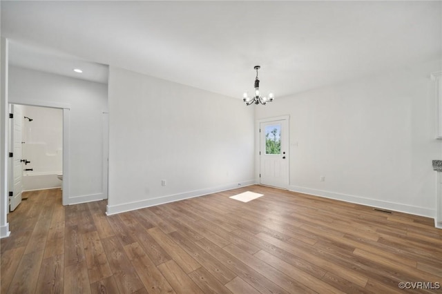 empty room featuring an inviting chandelier, recessed lighting, wood finished floors, and baseboards