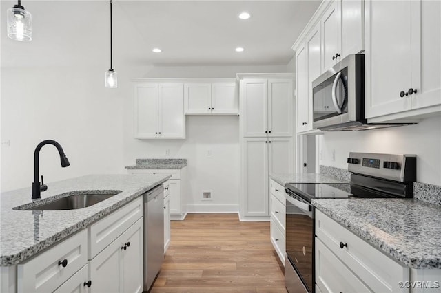 kitchen featuring light wood finished floors, pendant lighting, appliances with stainless steel finishes, white cabinetry, and a sink