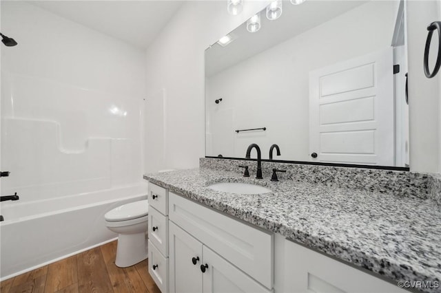 bathroom featuring vanity, toilet, wood finished floors, and shower / washtub combination