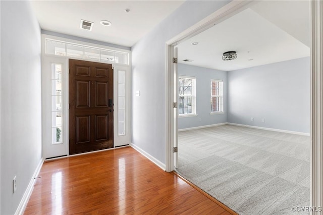 carpeted entrance foyer featuring visible vents, baseboards, and wood finished floors