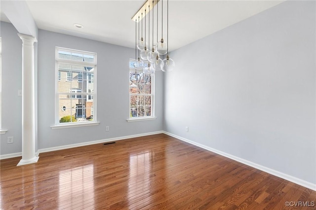 unfurnished dining area with wood finished floors, baseboards, and decorative columns