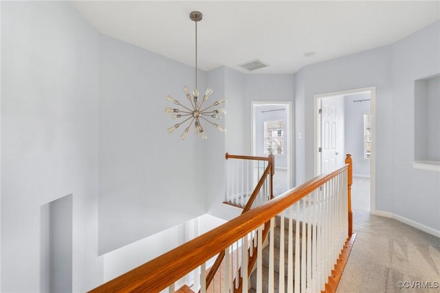 hall with visible vents, baseboards, an upstairs landing, a notable chandelier, and light colored carpet