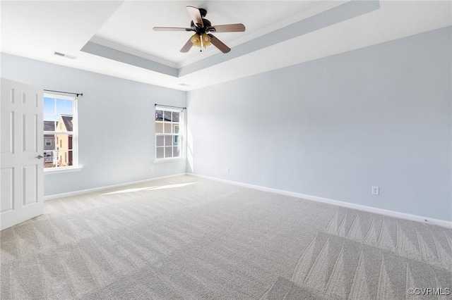 carpeted empty room featuring visible vents, baseboards, ceiling fan, crown molding, and a raised ceiling