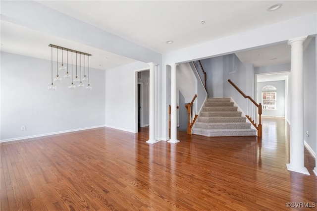 spare room with decorative columns, baseboards, wood finished floors, and stairs