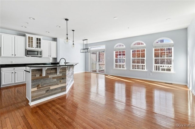 kitchen featuring dark countertops, stainless steel microwave, hardwood / wood-style floors, decorative backsplash, and white cabinets