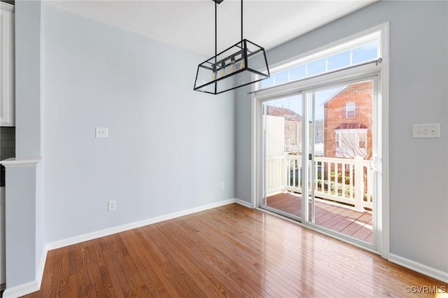 unfurnished dining area with a notable chandelier, wood finished floors, and baseboards