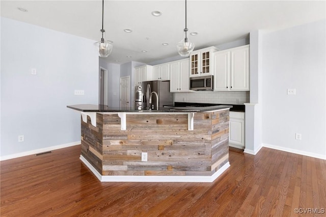 kitchen with a large island, dark wood-type flooring, dark countertops, appliances with stainless steel finishes, and decorative backsplash