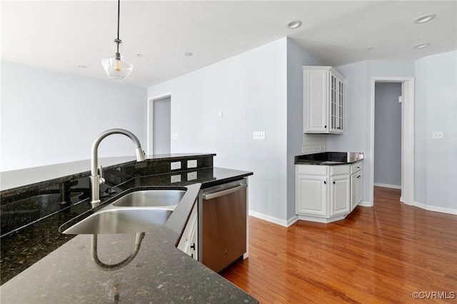 kitchen with a sink, stainless steel dishwasher, wood finished floors, white cabinets, and hanging light fixtures