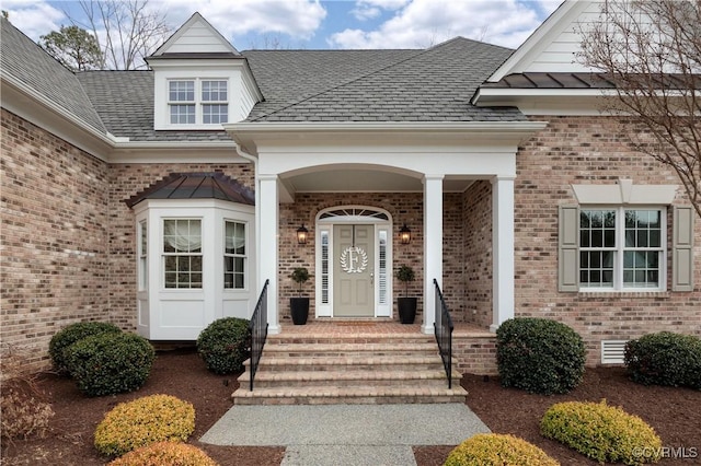 entrance to property featuring brick siding and a shingled roof