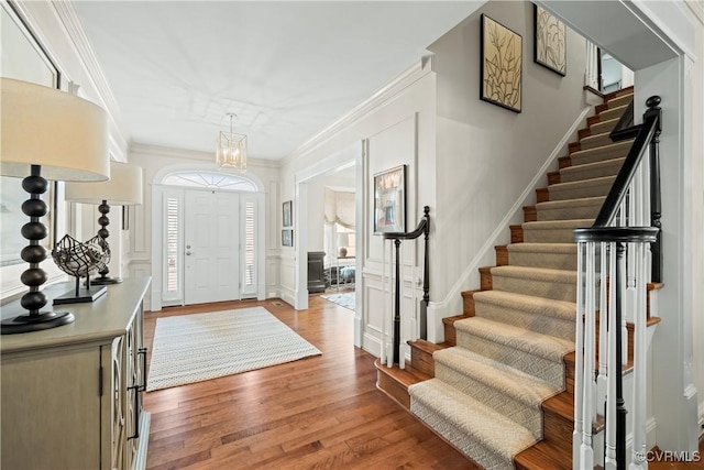 foyer entrance featuring ornamental molding, stairway, light wood-style floors, wainscoting, and a decorative wall