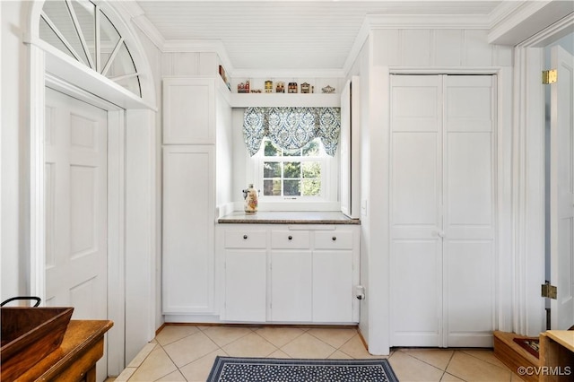 interior space with light tile patterned floors, stone countertops, ornamental molding, and white cabinetry