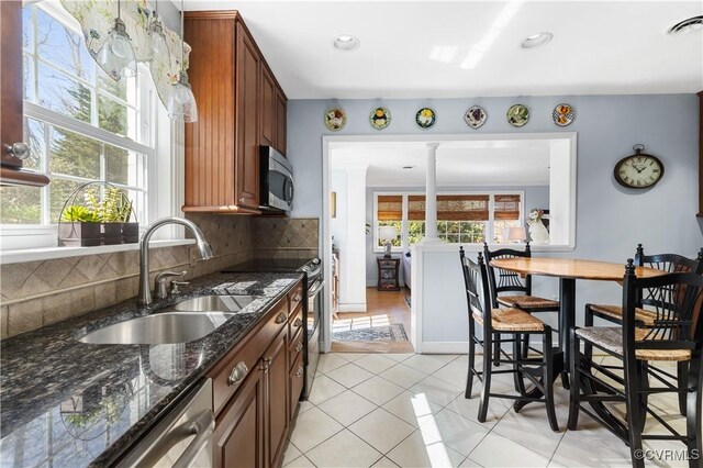 kitchen with a sink, decorative columns, stainless steel appliances, light tile patterned floors, and decorative backsplash