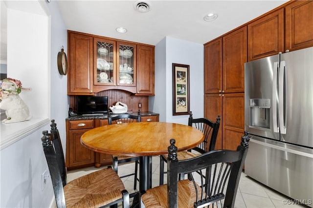 kitchen featuring light tile patterned floors, visible vents, glass insert cabinets, dark countertops, and stainless steel fridge