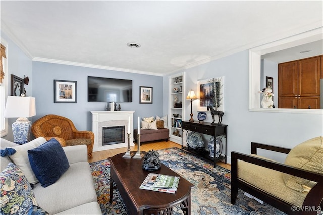 living room featuring built in shelves, light wood-style floors, a glass covered fireplace, and ornamental molding