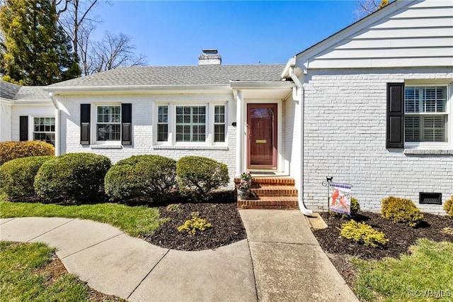 entrance to property featuring crawl space, brick siding, roof with shingles, and a chimney