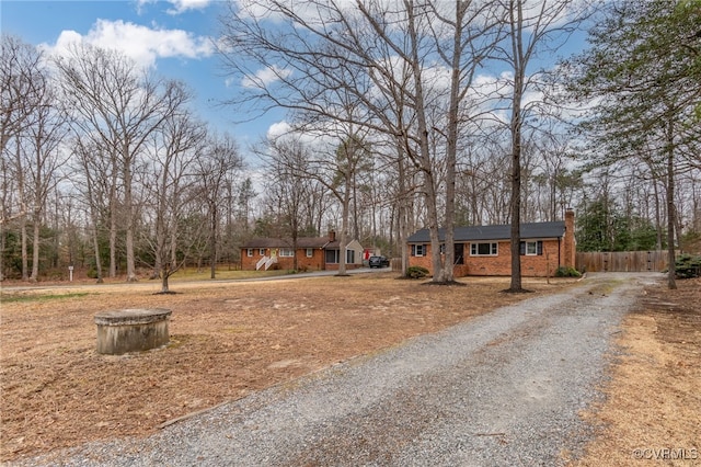 view of front of home featuring brick siding, driveway, a chimney, and fence