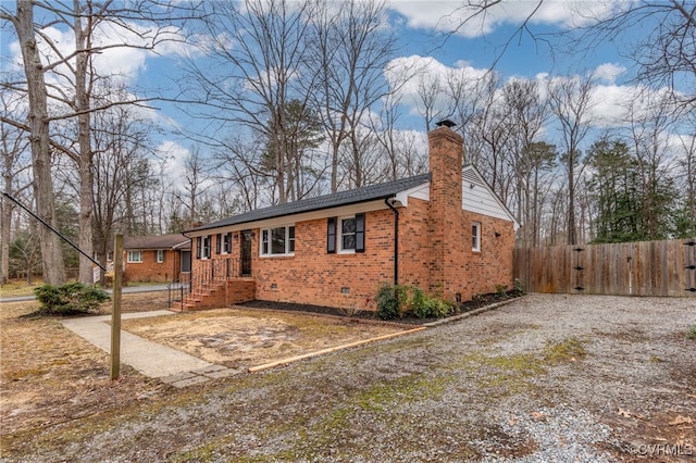 view of front of property with brick siding, a chimney, crawl space, fence, and driveway