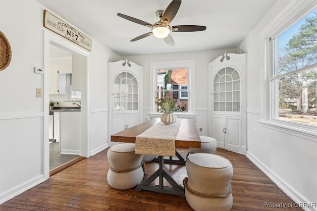 dining area with dark wood-style floors, wainscoting, a ceiling fan, and baseboards