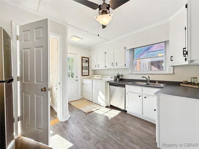 kitchen featuring light wood finished floors, washer and clothes dryer, dark countertops, stainless steel appliances, and a sink