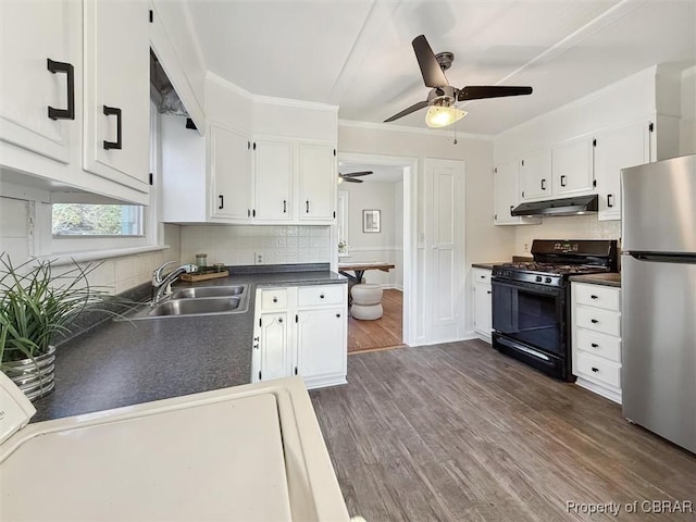 kitchen with under cabinet range hood, a sink, gas stove, freestanding refrigerator, and dark countertops