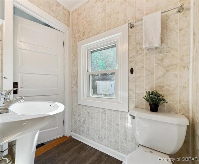 bathroom featuring baseboards, wood finished floors, toilet, and tile walls