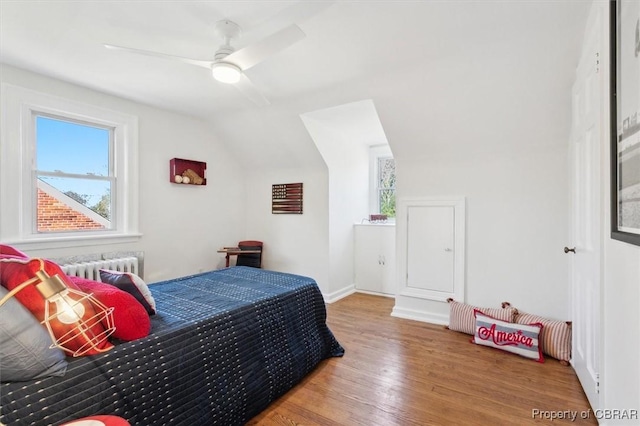 bedroom with vaulted ceiling, wood finished floors, and radiator