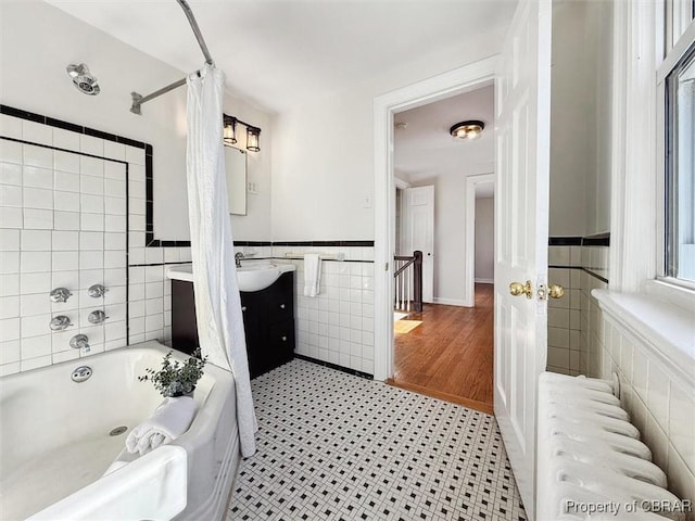 bathroom featuring tile walls, shower / bath combination with curtain, radiator heating unit, wainscoting, and vanity