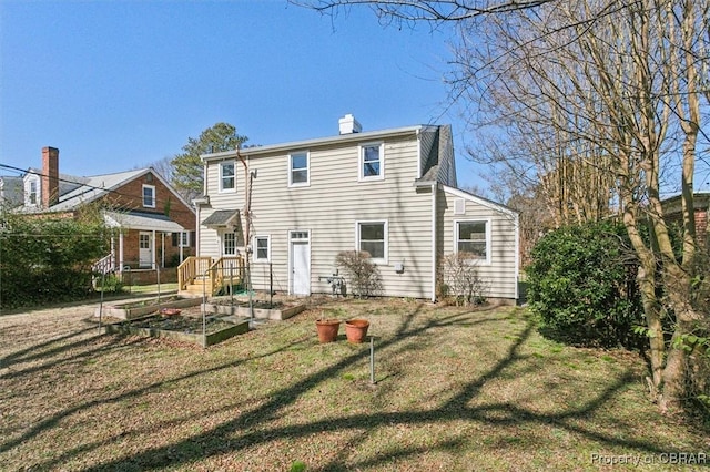 rear view of house with a lawn, a chimney, and a vegetable garden