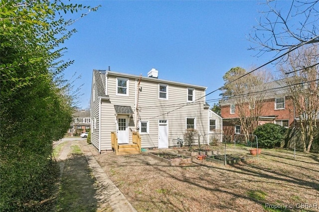 rear view of house with a lawn, a chimney, and a vegetable garden