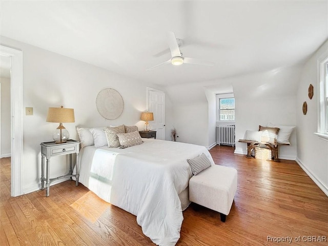 bedroom featuring a ceiling fan, radiator, baseboards, and light wood finished floors