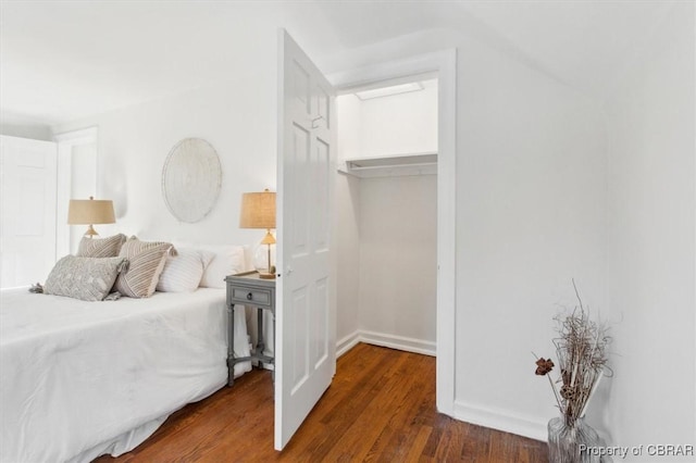 bedroom featuring a walk in closet, a closet, baseboards, and wood finished floors