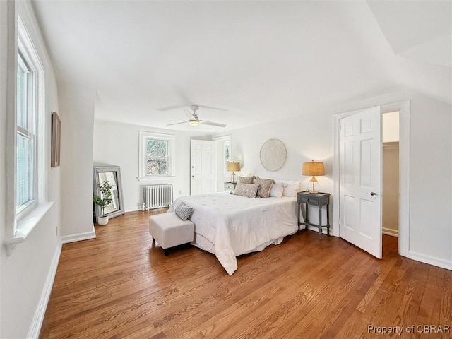 bedroom with light wood-style floors, radiator, ceiling fan, and baseboards