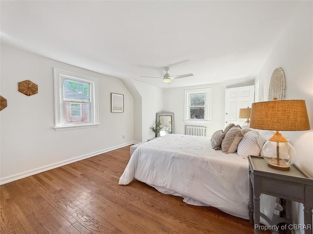 bedroom featuring radiator heating unit, multiple windows, baseboards, and wood finished floors