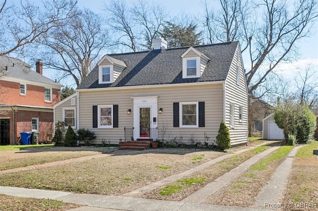 cape cod home featuring driveway, a shingled roof, a chimney, an outbuilding, and a front yard