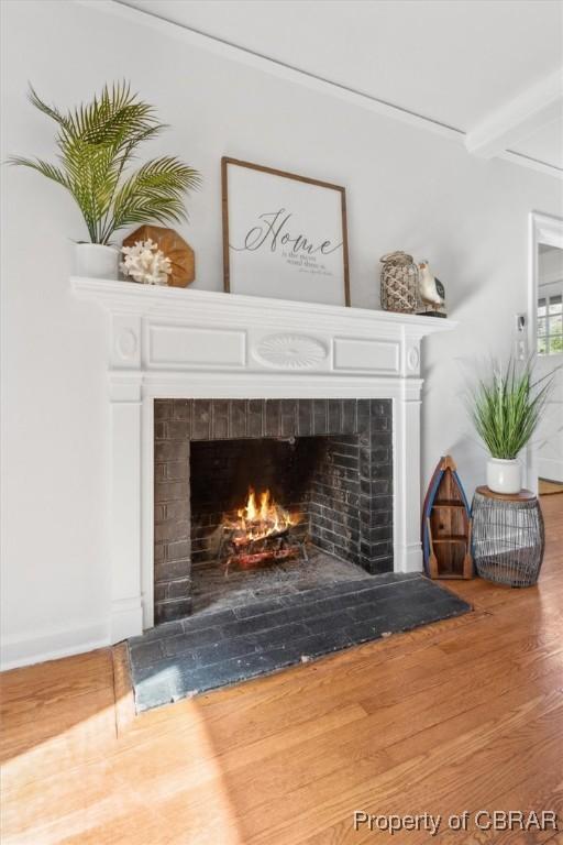 room details with a lit fireplace, beamed ceiling, and wood finished floors