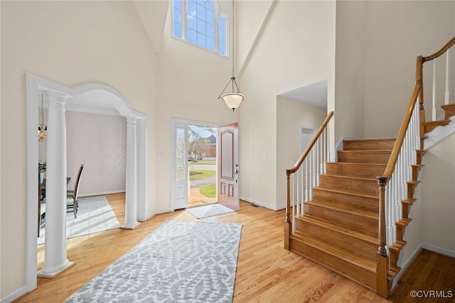 foyer with arched walkways, ornate columns, light wood-style floors, baseboards, and stairs