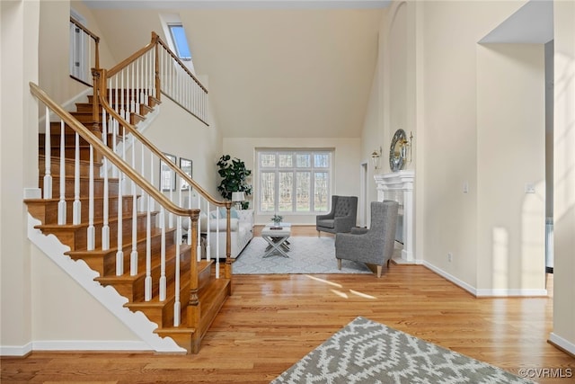 foyer featuring high vaulted ceiling, a fireplace, wood finished floors, baseboards, and stairs