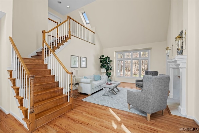 living room featuring a skylight, wood finished floors, a towering ceiling, baseboards, and stairs