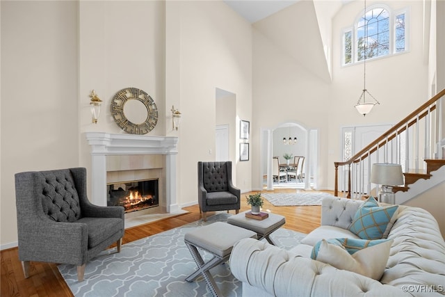 living room with arched walkways, stairway, a tiled fireplace, and wood finished floors