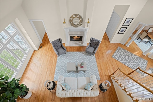 living area featuring stairs, wood finished floors, a glass covered fireplace, and a towering ceiling