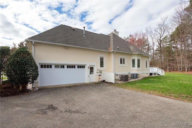 exterior space featuring a yard, a chimney, a shingled roof, central AC unit, and driveway