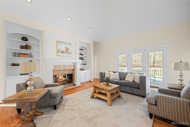 living area featuring built in shelves, recessed lighting, french doors, light wood-type flooring, and a tiled fireplace